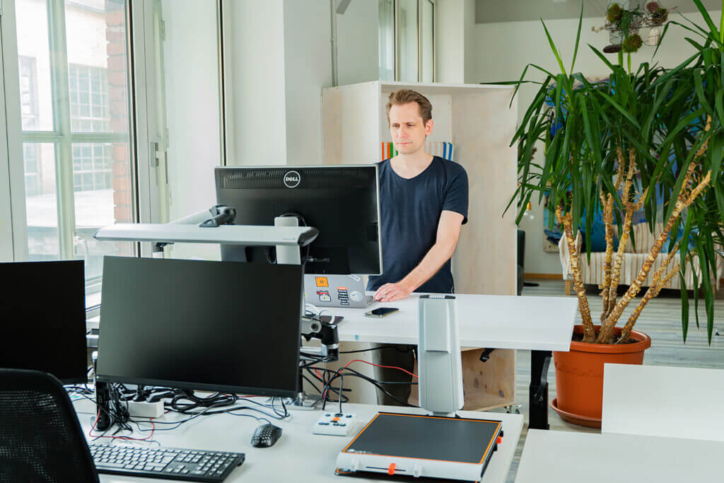ein Mann in einer Büroumgebung steht an einem höhenverstellbaren Schreibtisch mit Monitor